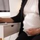pregnant woman, office chair writing at desk.