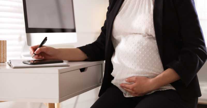 pregnant woman, office chair writing at desk.