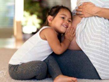 older child with ear on mom's pregnant belly.