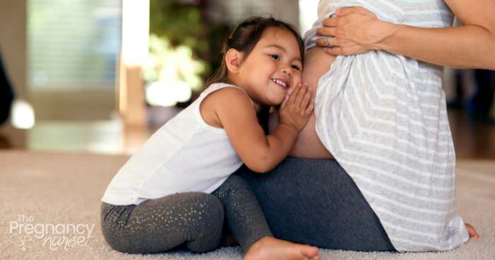 older child with ear on mom's pregnant belly.