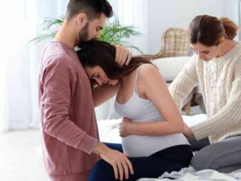 husband holding pregnant wife in pain with doula behind her.