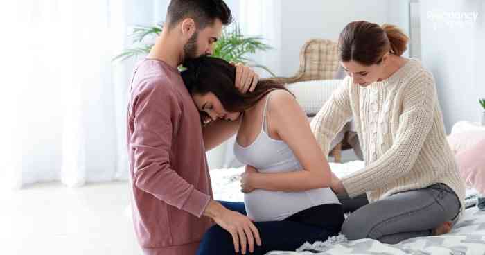husband holding pregnant wife in pain with doula behind her.